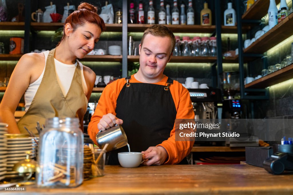 Junger Mann mit Down-Syndrom arbeitet im Café und bereitet Kaffee zu