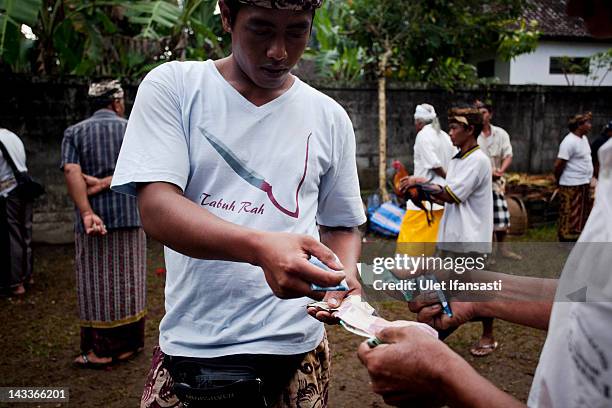 Balinese men make a transaction at the end of a cockfight during the sacred 'Aci Keburan' ritual at Nyang Api Temple on February 16, 2012 in Gianyar,...