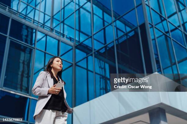confident young asian businesswoman with smart phone on the move - bank building exterior stock pictures, royalty-free photos & images