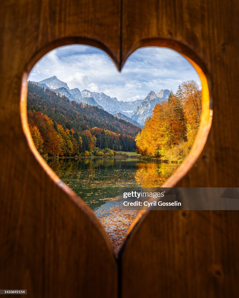 Rießersee and Wetterstein mountain range in autumn, through heart shaped opening in window shutter