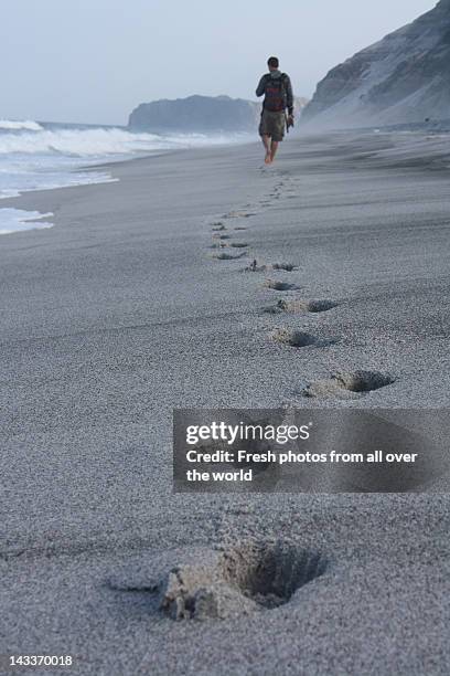 boy walking on beach leaving footprints in sand - one man only stock pictures, royalty-free photos & images