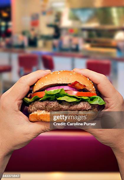 man holding a hamburger in a diner - burgers stockfoto's en -beelden