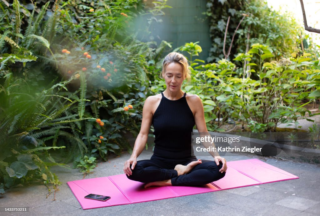Woman meditating in the garden, sitting cross-legged on exercise mat