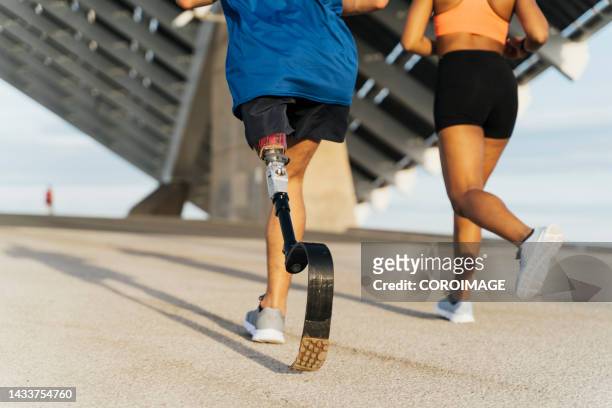 vista trasera de una pareja haciendo footing con un panel solar en el fondo. concepto de discapacidad e inclusión. - künstliches gliedmaß stock-fotos und bilder