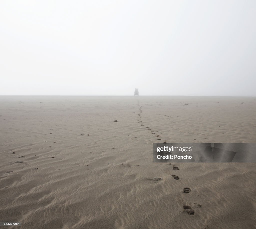 Footprints at beach with off road car in the fog