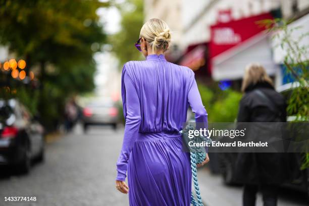 Leonie Hanne wears purple cat eyes sunglasses, a purple turtleneck / long sleeves / wrap pleated midi dress, a pale blue matte leather / chains...