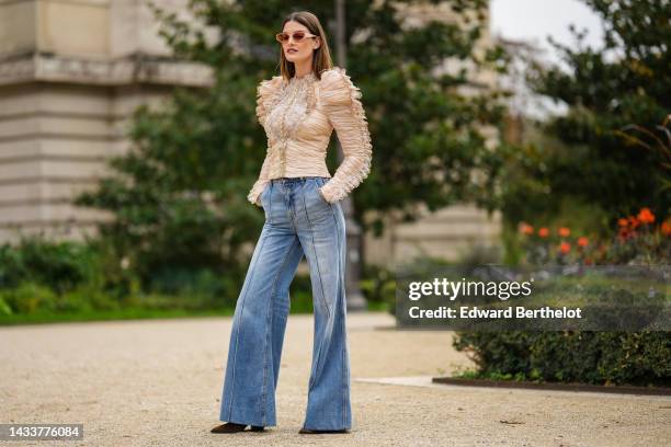 Ophelie Guillermand wears beige sunglasses, a beige tulle pleated / embroidered lace pattern / shoulder-pads / long sleeves blouse, a brown shiny...