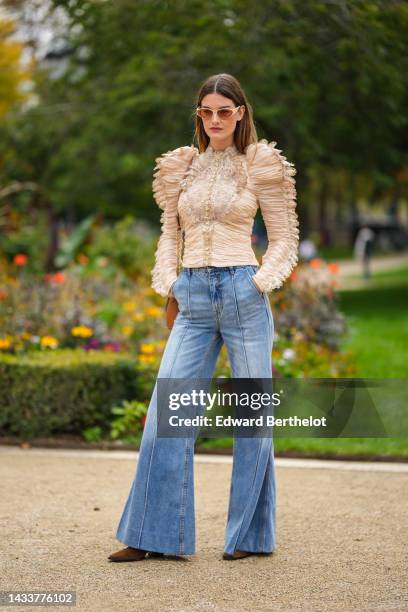 Ophelie Guillermand wears beige sunglasses, a beige tulle pleated / embroidered lace pattern / shoulder-pads / long sleeves blouse, a brown shiny...