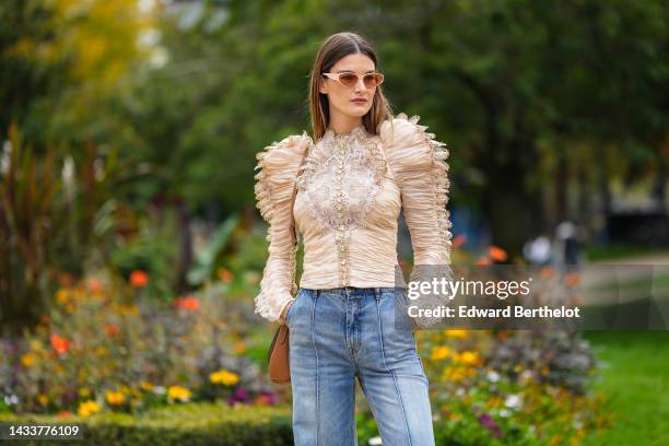 Ophelie Guillermand wears beige sunglasses, a beige tulle pleated / embroidered lace pattern / shoulder-pads / long sleeves blouse, a brown shiny...