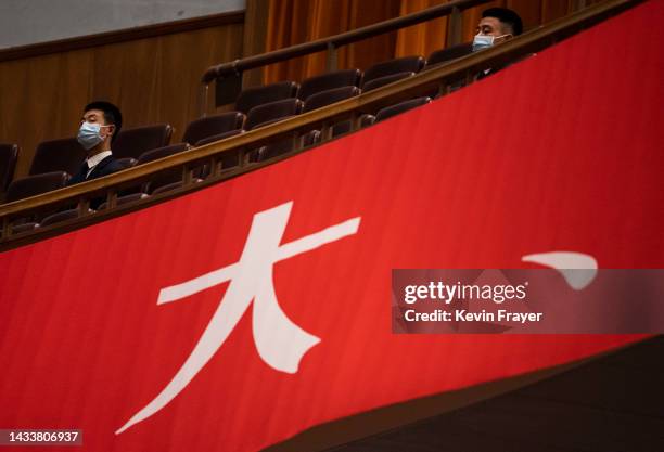 Ushers sit near a banner in the seating area during the Opening Ceremony of the 20th National Congress of the Communist Party of China at The Great...