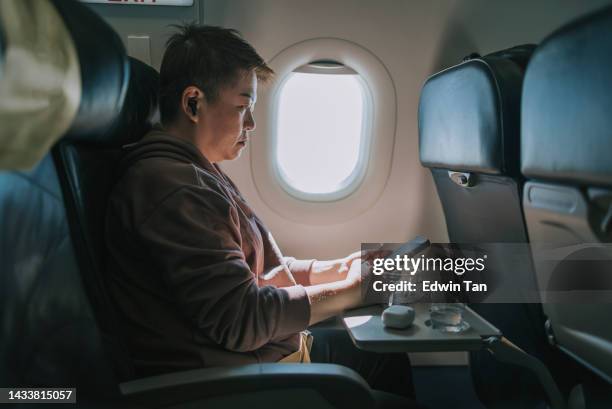 asiatische chinesin mit smartphone auf dem beifahrerfenstersitz im flugzeug sitzend - airplane tray stock-fotos und bilder