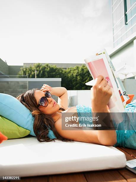 mixed race woman sunbathing and reading magazine - mixed magazine stock-fotos und bilder