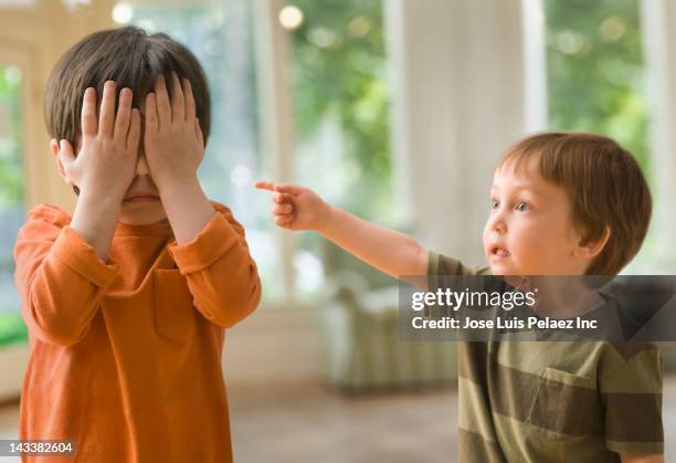 mixed race boy pointing at brother who's covering his eyes - verwijten stockfoto's en -beelden