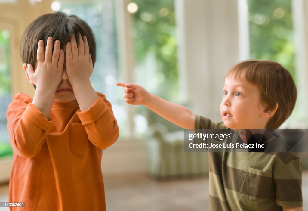 Mixed race boy pointing at brother who's covering his eyes