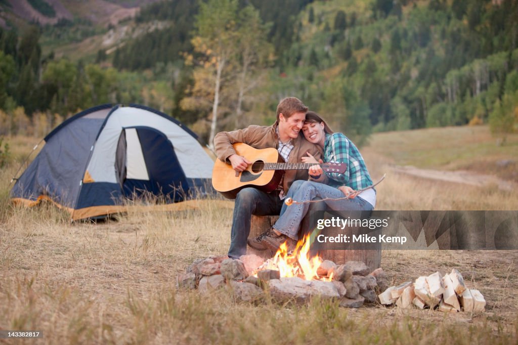 Caucasian man playing guitar for wife near campfire