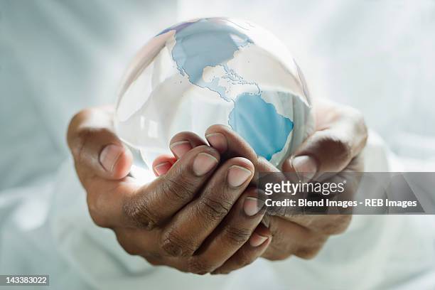mixed race man holding glass globe - hohle hände stock-fotos und bilder