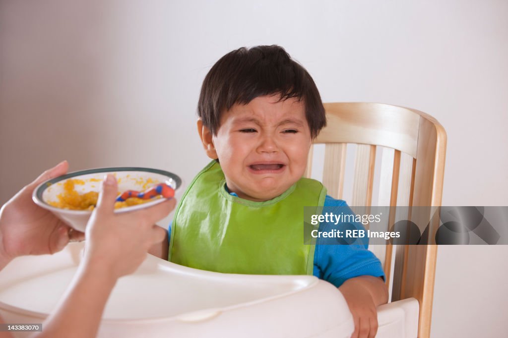 Hispanic mother trying to feed crying baby boy