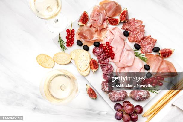 two glasses of white wine with cheese and salami olives berries. - charcuterie board 個照片及圖片檔