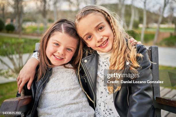 close-up view of two young girls smiling while embracing each other sitting on a park bench. - alleen kinderen stockfoto's en -beelden
