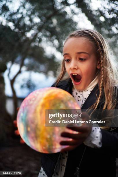 amazed young girl with her mouth open looking at a colorful illuminated sphere while standing outdoors in a park. - man made space fotografías e imágenes de stock