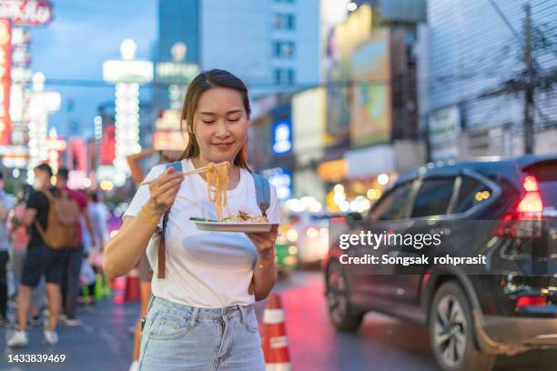 young asian tourist woman eating pad thai noodle, traditional street food in thailand and looking far away - female octopus stock-fotos und bilder