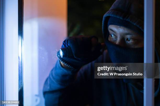 criminal concept the masked thief peeped into the house through a glass door or an open window. - bandit stock pictures, royalty-free photos & images