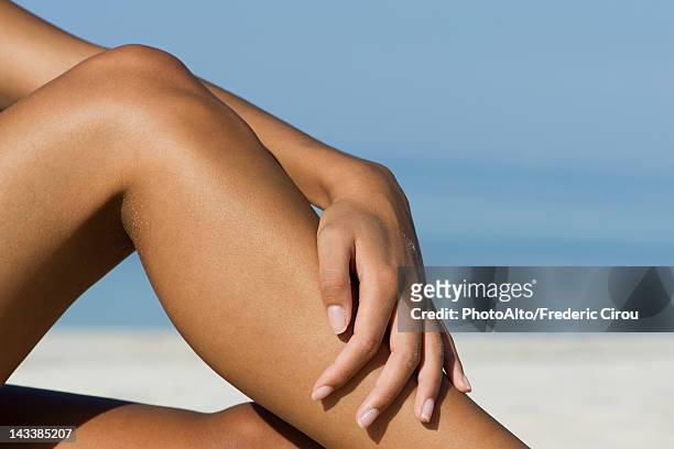woman touching bare legs at the beach, cropped - braun stock-fotos und bilder