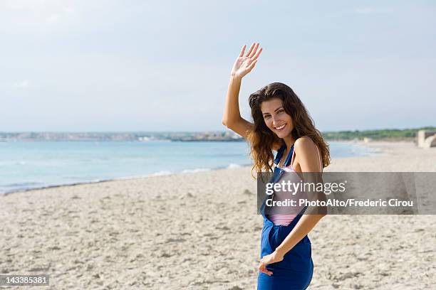 young woman at the beach, smiling and waving at camera - waving imagens e fotografias de stock