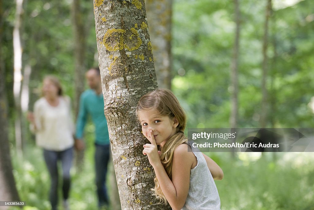 Girl hiding behind tree with finger on lips
