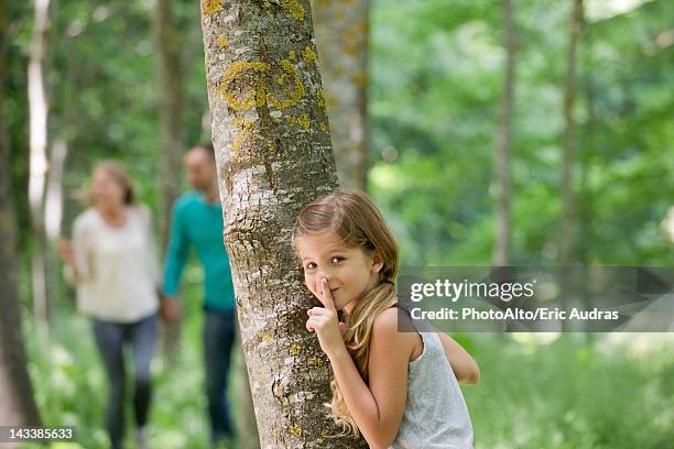 girl hiding behind tree with finger on lips - hidw and seek stock pictures, royalty-free photos & images