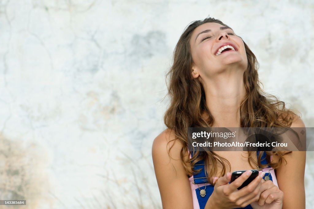 Young woman holding cell phone, laughing