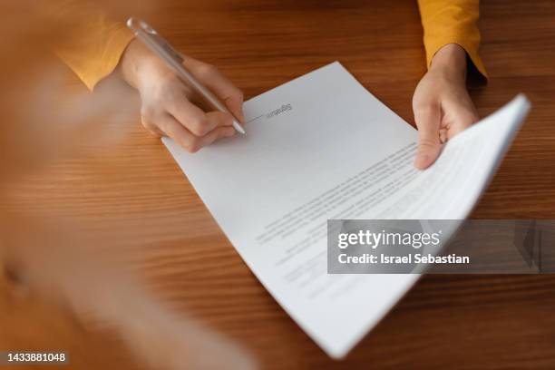 close up image of an unrecognizable person's hands signing a business document on a wooden desk. business concept. - contrato fotografías e imágenes de stock