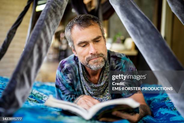 mature man lying on flying bed and reading a book - barba incolta foto e immagini stock