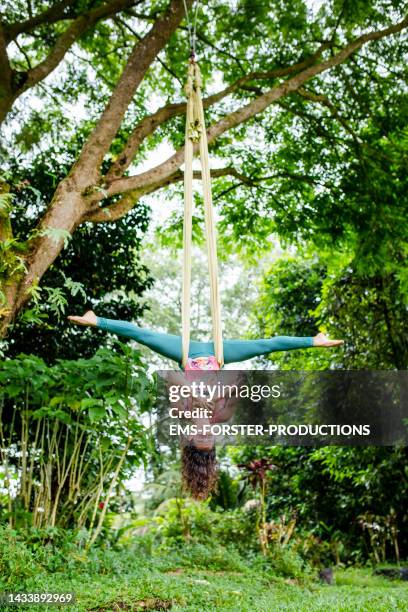 young woman practicing aerial yoga or fly yoga outdoors in the garden rainforest - rainforest garden stock-fotos und bilder