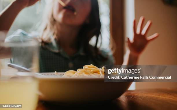 a child slurps spaghetti in the background as focus falls on a full bowl of pasta - dining table stock pictures, royalty-free photos & images