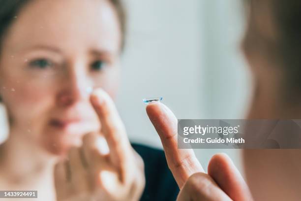 woman with contact lens in mirror. - lens eye stock-fotos und bilder