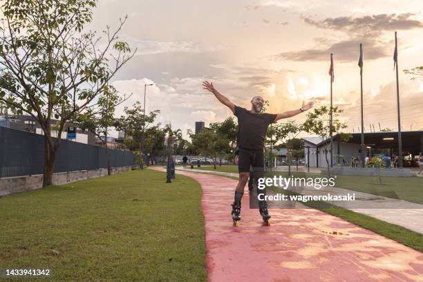 man skating in public park with arms outstretched - inline skating man park stock pictures, royalty-free photos & images