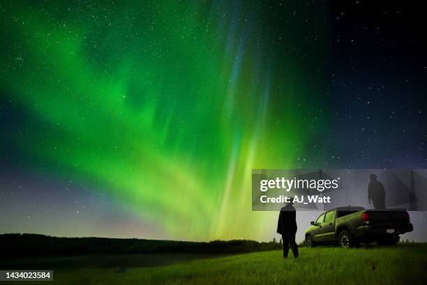 couple standing by their pick-up truck watching aurora borealis - aurora borealis stock pictures, royalty-free photos & images
