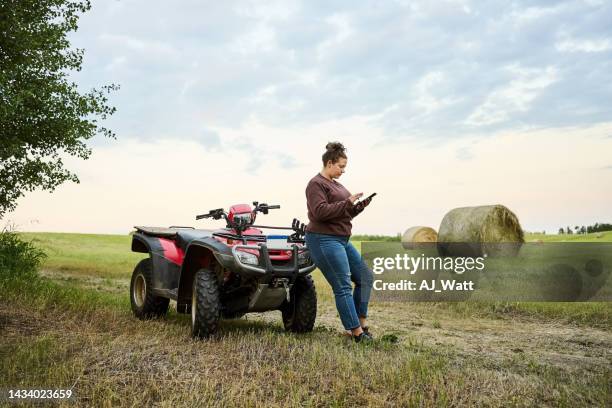 female farmer using mobile phone leaning to atv on the farm field - hay stock pictures, royalty-free photos & images