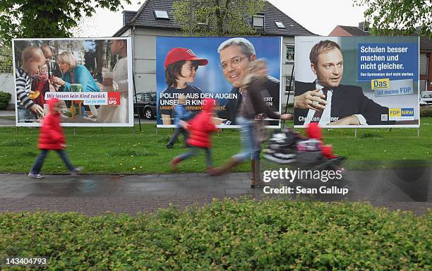 Woman and children walk past state election campaign posters for Social Democrat Hannelore Kraft, Christian Democrat Norbert Roettgen and Free...