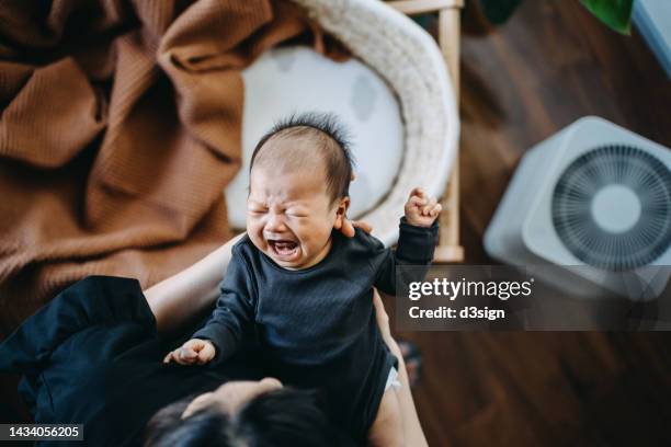 high angle shot of loving young asian mother carrying her crying newborn baby daughter in arms, consoling and comforting her. hunger and discomfort. motherhood, parenthood concept - moms crying in bed stock pictures, royalty-free photos & images