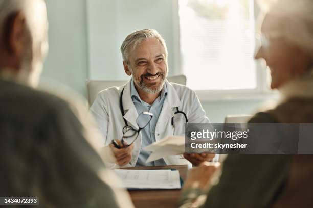 glücklicher arzt, der während eines termins im büro mit seinen patienten spricht. - hausarzt stock-fotos und bilder