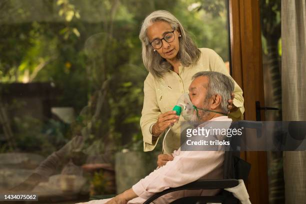 donna che applica la maschera di ossigeno al vecchio marito sulla sedia a rotelle - apparecchio per la respirazione foto e immagini stock