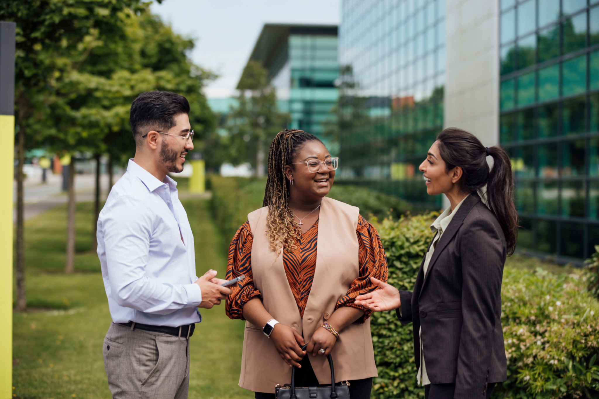 A waist-up shot of three colleagues talking outside of the office during working hours. They are all smartly dressed talking and laughing with each other. Located in the North East of England.