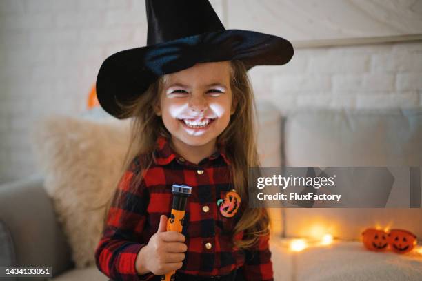 toddler girl, dressed as a witch for a halloween, making a spooky face with a flashlight - flashlight stock pictures, royalty-free photos & images