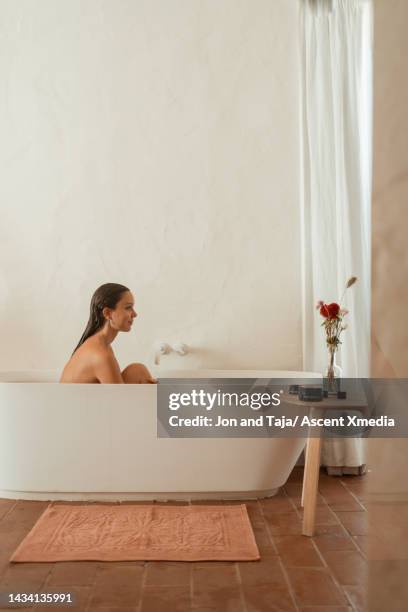 young woman relaxes in bathtub in modern bathroom - bathmat stock pictures, royalty-free photos & images