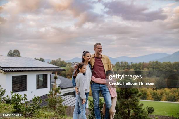 cheerful family standing and posing in front of their house with solar panels. alternative energy, saving resources and sustainable lifestyle concept. - public building stock photos et images de collection