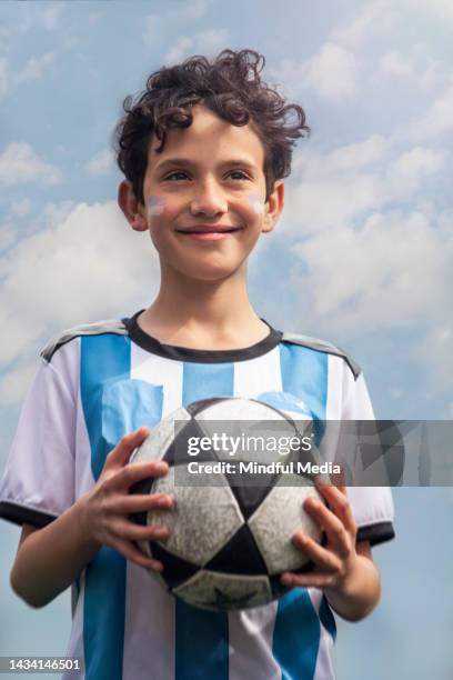 retrato a mitad de plano de un joven argentino sonriente con la camiseta del equipo nacional de fútbol mientras sostiene el fútbol en las manos - futbol argentino fotografías e imágenes de stock