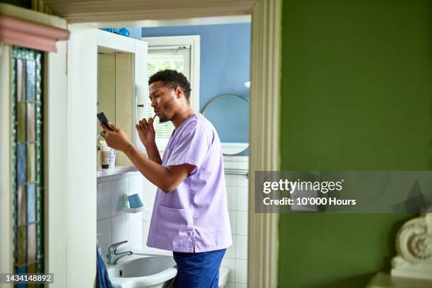 young black care worker brushing teeth and checking phone - brush teeth phone stock-fotos und bilder