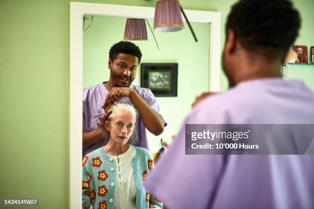 reflection of male care worker brushing senior woman's hair - vulnerability stock pictures, royalty-free photos & images